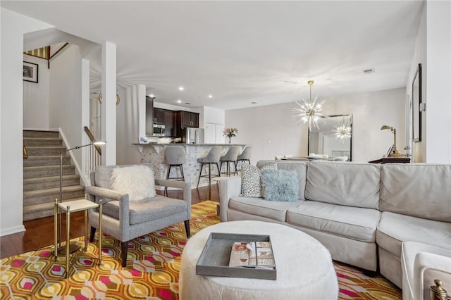 living room featuring an inviting chandelier, stairs, wood finished floors, and recessed lighting