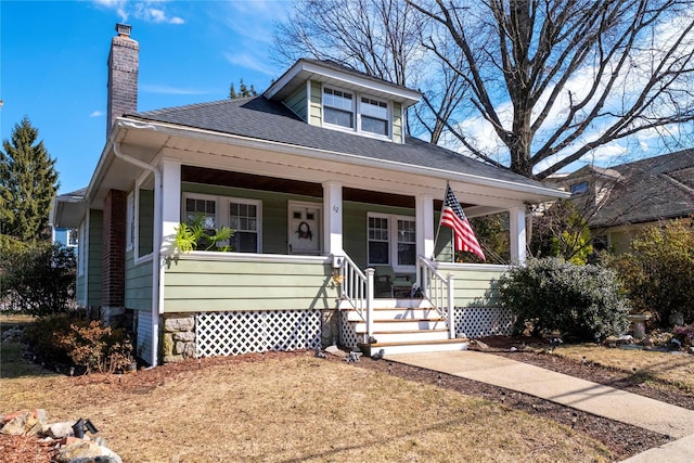 bungalow-style house featuring a shingled roof, covered porch, and a chimney