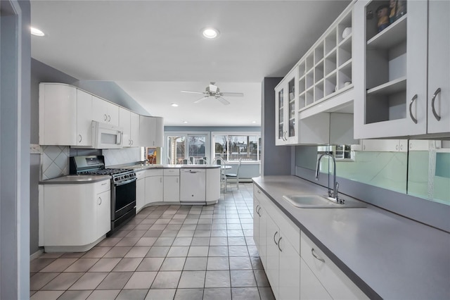 kitchen featuring decorative backsplash, white microwave, white cabinetry, a sink, and gas stove