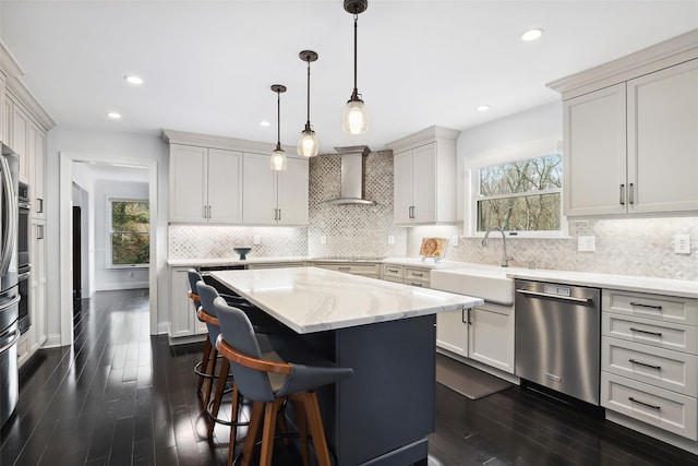 kitchen featuring backsplash, stainless steel dishwasher, a kitchen island, a sink, and wall chimney range hood