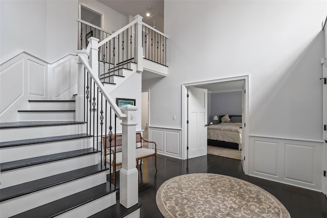 stairs featuring a high ceiling, wainscoting, wood finished floors, and a decorative wall