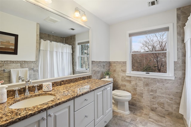 bathroom with toilet, visible vents, tile walls, and vanity