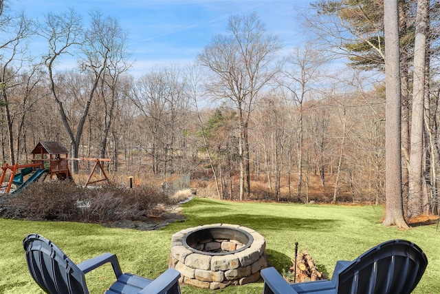 view of yard with a playground, a fire pit, and a forest view