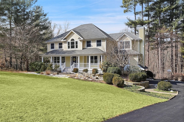 view of front of home featuring driveway, a chimney, roof with shingles, covered porch, and a front yard