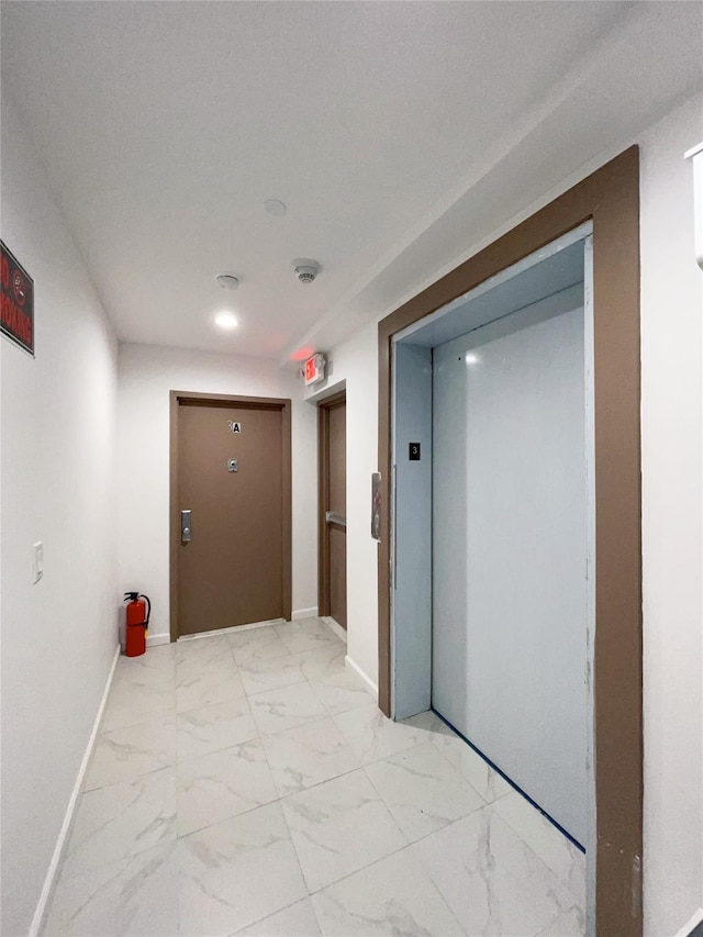 corridor featuring marble finish floor, elevator, and baseboards