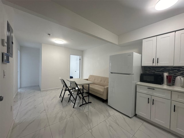 kitchen with black microwave, marble finish floor, light countertops, backsplash, and freestanding refrigerator