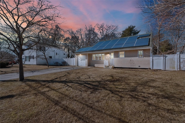 view of front of home featuring a lawn, fence, a gate, and roof mounted solar panels