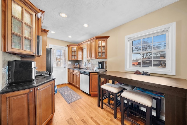 kitchen with a sink, light wood-type flooring, backsplash, dishwasher, and brown cabinetry