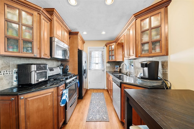 kitchen featuring decorative backsplash, brown cabinetry, appliances with stainless steel finishes, light wood-type flooring, and a sink