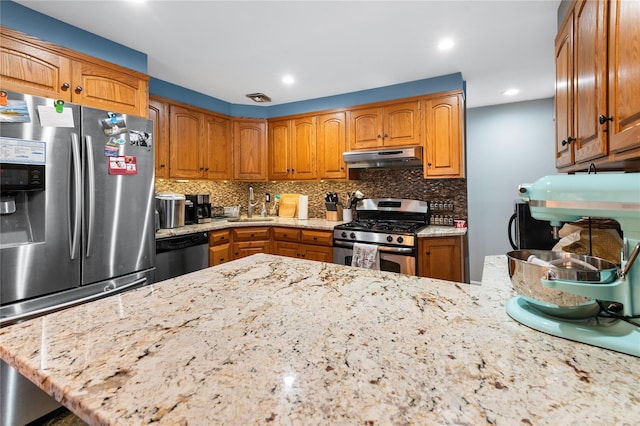 kitchen with under cabinet range hood, a peninsula, appliances with stainless steel finishes, backsplash, and light stone countertops