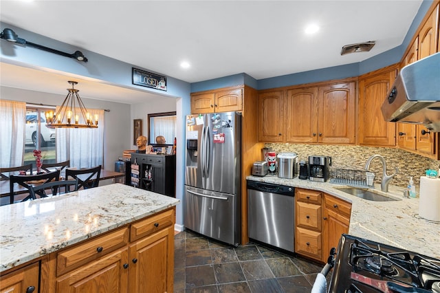 kitchen with a chandelier, light stone counters, a sink, appliances with stainless steel finishes, and decorative backsplash