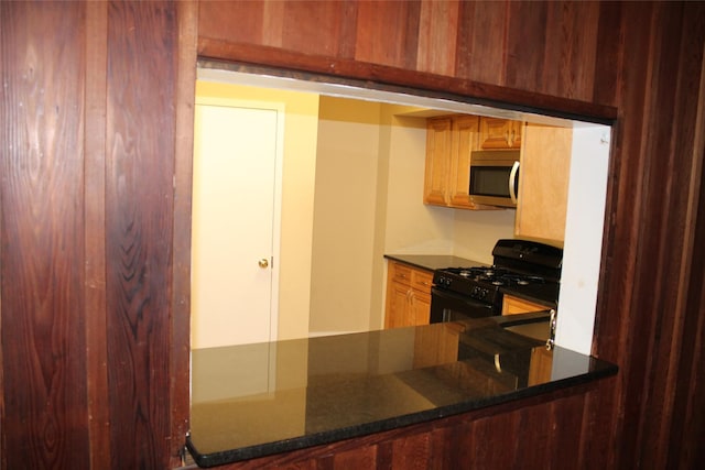 kitchen with black range with gas cooktop, stainless steel microwave, and dark stone countertops