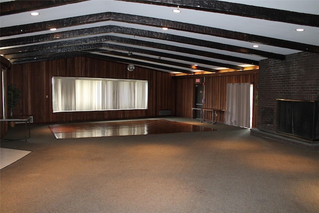 unfurnished living room featuring lofted ceiling with beams, wood walls, a brick fireplace, and carpet flooring