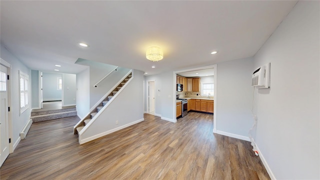 unfurnished living room featuring recessed lighting, a baseboard heating unit, wood finished floors, baseboards, and stairs