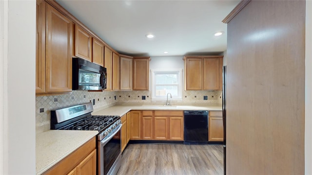 kitchen featuring light countertops, a sink, light wood-style flooring, and black appliances