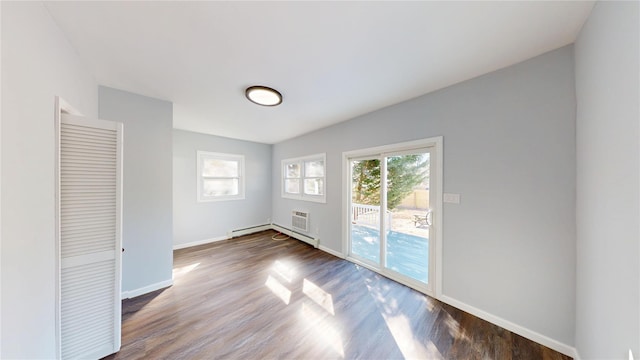 spare room with a baseboard heating unit, a wall mounted air conditioner, baseboards, and wood finished floors