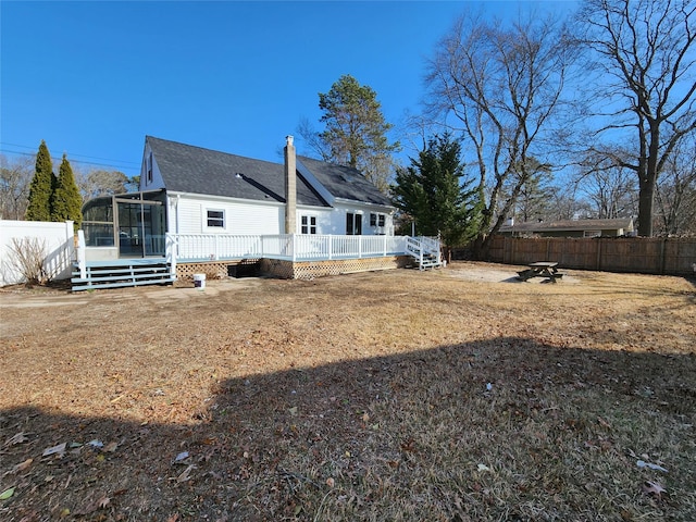 rear view of house featuring roof with shingles, a chimney, a sunroom, a fenced backyard, and a wooden deck