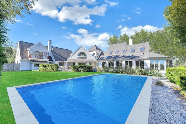 rear view of house with a balcony, fence, an outdoor pool, a chimney, and a lawn