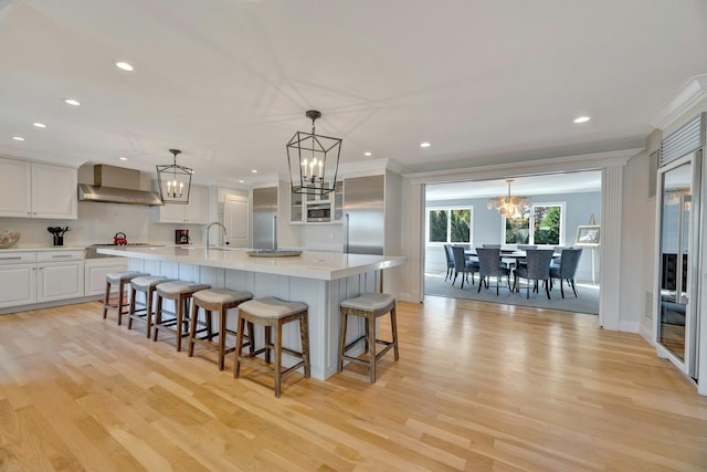 kitchen featuring light wood-style flooring, light countertops, stainless steel gas stovetop, wall chimney range hood, and a chandelier