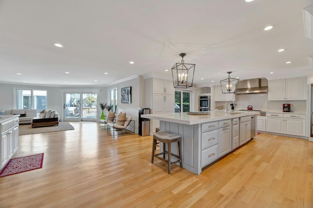 kitchen featuring open floor plan, stainless steel oven, white cabinetry, wall chimney exhaust hood, and a sink