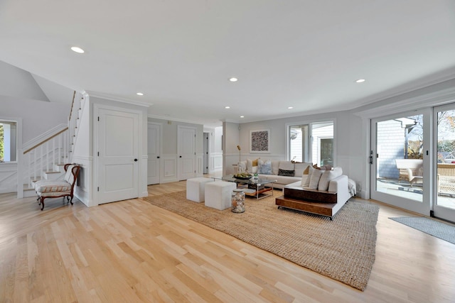 living room with stairs, a wainscoted wall, light wood-type flooring, and ornamental molding