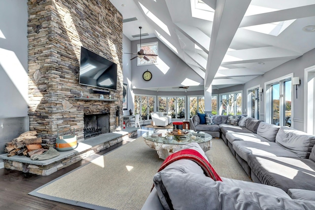 living room featuring a stone fireplace, a skylight, wood finished floors, and a ceiling fan