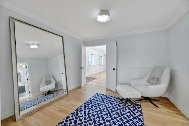 sitting room with crown molding, a decorative wall, wood finished floors, and a wainscoted wall