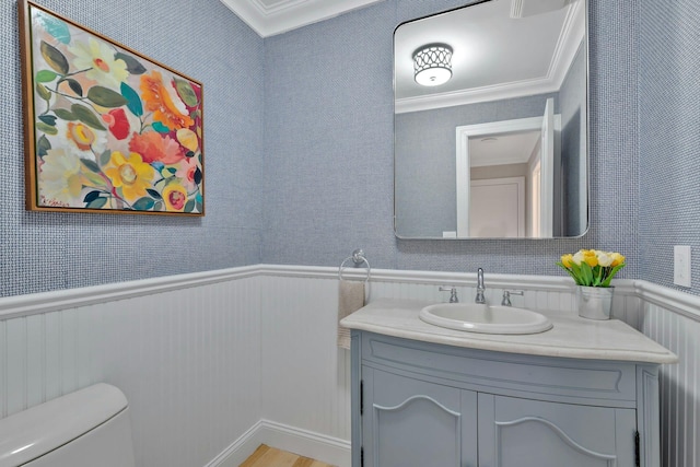 bathroom with a wainscoted wall, toilet, vanity, and crown molding