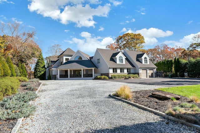 shingle-style home featuring a garage, driveway, a standing seam roof, stone siding, and metal roof