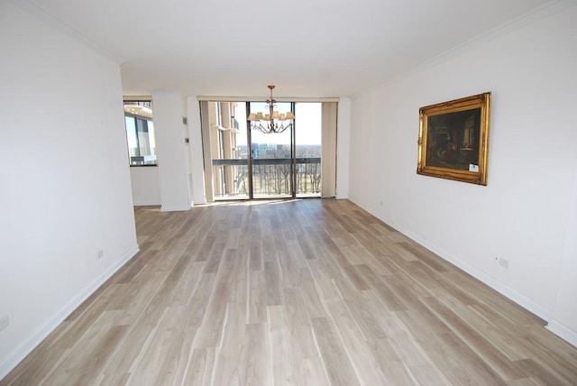 unfurnished room with a chandelier, light wood-style flooring, baseboards, expansive windows, and crown molding