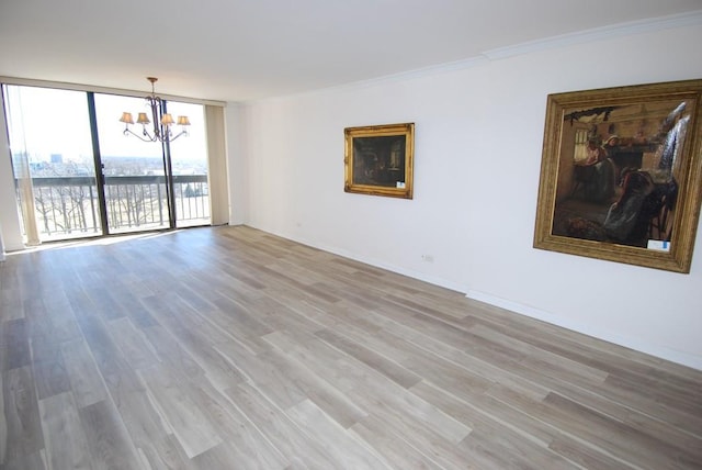 spare room with baseboards, ornamental molding, wood finished floors, an inviting chandelier, and a wall of windows