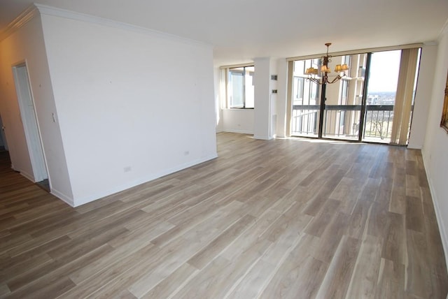 unfurnished living room with light wood-style flooring, ornamental molding, a chandelier, and baseboards