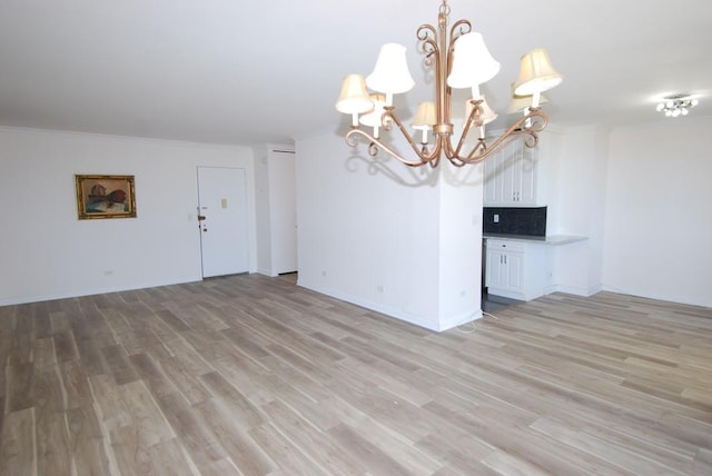 unfurnished living room with ornamental molding, light wood finished floors, baseboards, and a notable chandelier