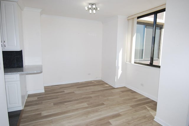 unfurnished dining area featuring light wood-type flooring, baseboards, and ornamental molding