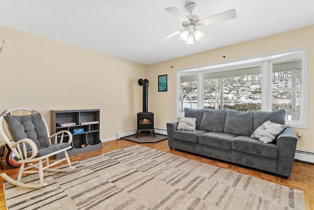 living room with a wood stove, a baseboard radiator, baseboards, and ceiling fan