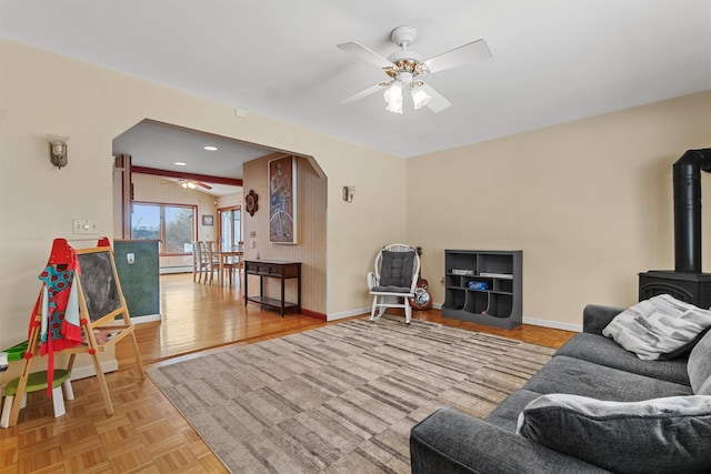 living room featuring ceiling fan, arched walkways, baseboards, parquet floors, and a wood stove