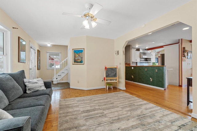 living area with baseboards, arched walkways, a ceiling fan, stairway, and parquet flooring