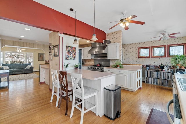 kitchen featuring light wood-style floors, white cabinetry, wall chimney range hood, stainless steel gas range oven, and wallpapered walls