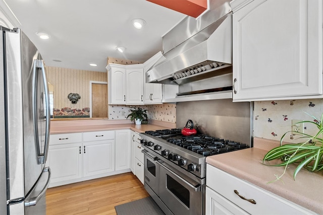 kitchen featuring light countertops, appliances with stainless steel finishes, wall chimney range hood, and white cabinets