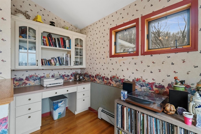 office space featuring a baseboard radiator, vaulted ceiling, light wood-type flooring, built in study area, and wallpapered walls