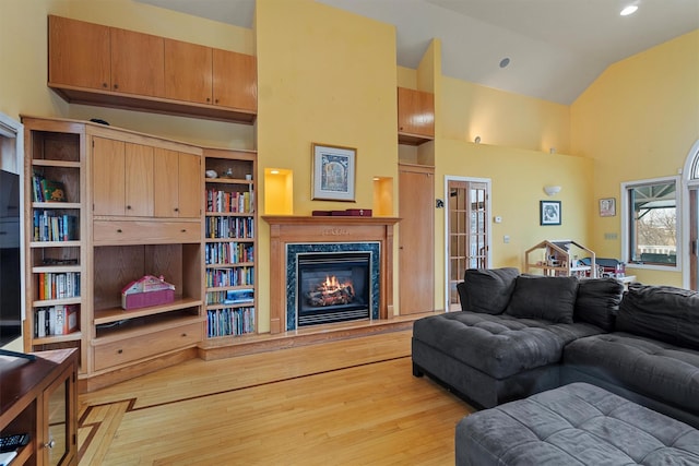 living area with high vaulted ceiling, a premium fireplace, and wood finished floors