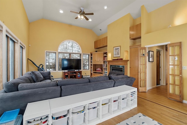 living area with ceiling fan, high vaulted ceiling, recessed lighting, a high end fireplace, and light wood-style floors