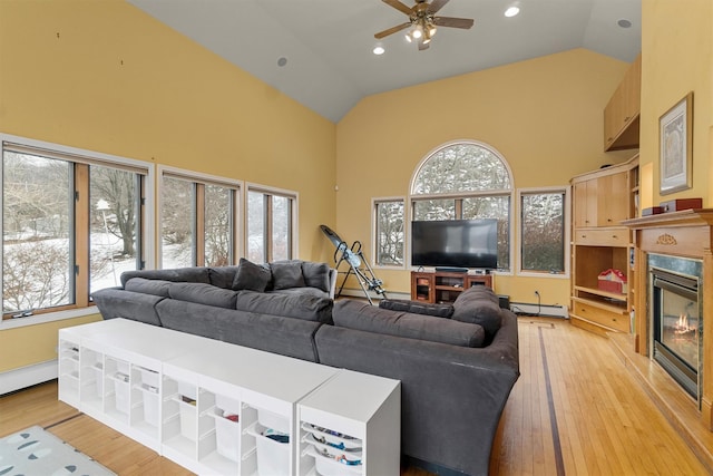 living room with high vaulted ceiling, a glass covered fireplace, and light wood-style floors