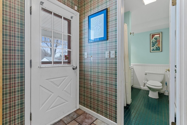 full bath featuring a wainscoted wall, tile patterned flooring, toilet, and wallpapered walls