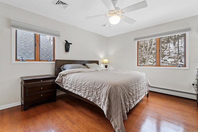 bedroom with ceiling fan, a baseboard radiator, hardwood / wood-style flooring, visible vents, and baseboards