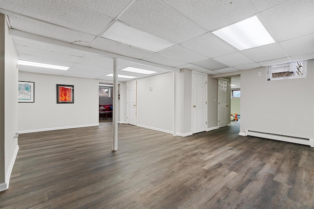 below grade area with a baseboard heating unit, a drop ceiling, baseboards, and wood finished floors