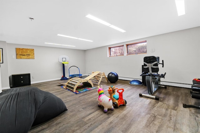 exercise area featuring a baseboard heating unit, baseboards, and wood finished floors