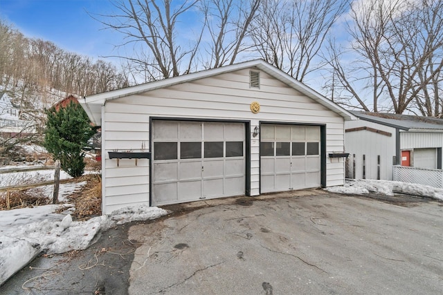 snow covered garage with a detached garage and fence