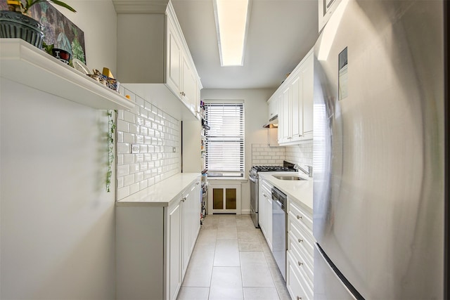 kitchen with light tile patterned floors, stainless steel appliances, a sink, light countertops, and backsplash