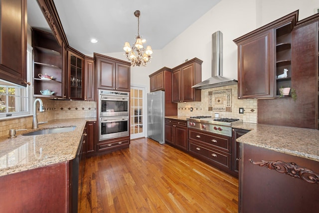 kitchen featuring appliances with stainless steel finishes, open shelves, a sink, a notable chandelier, and wall chimney exhaust hood